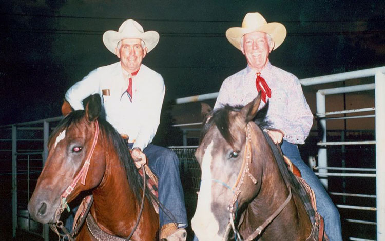 Older photo of two cowboys on horses in the evening.